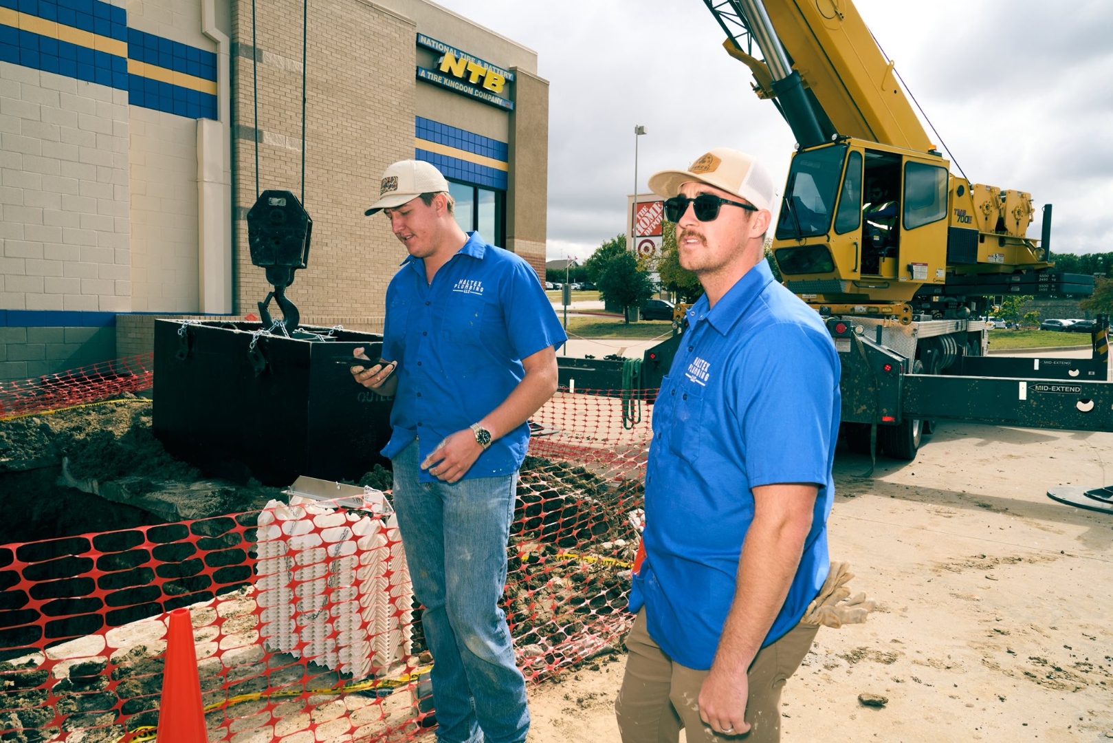Two Haltex crew members at a commercial job site with crane for grease trap installation